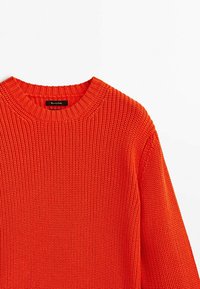 Pull en tricot épais de couleur orange vif. Il présente un col rond côtelé et un tissu texturé. Étiquette visible à l'intérieur du col.