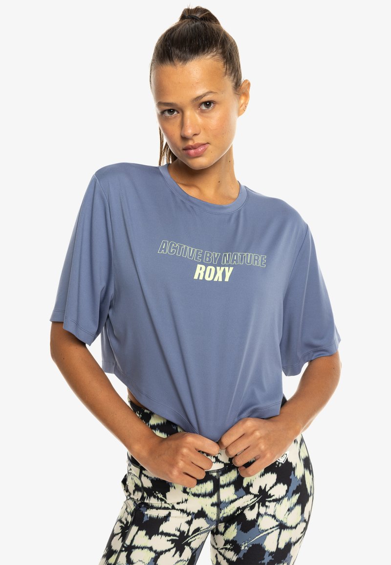 Light blue cropped t-shirt with short sleeves and a crew neckline. The front features text "ACTIVE BY NATURE" and "ROXY" in contrasting colors.