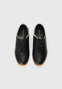 Black leather sneakers with a textured finish, featuring a cream-colored collar, black laces, and a gum rubber sole. Logo on tongue.