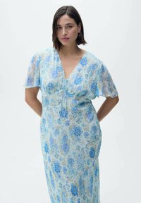 Leicht fließendes, hellblaues Kleid mit floralem Muster in dunkleren Blautönen. Verfügt über kurze Schmetterlingsärmel, einen V-Ausschnitt und ein Kordelzugdetail im Oberteil.