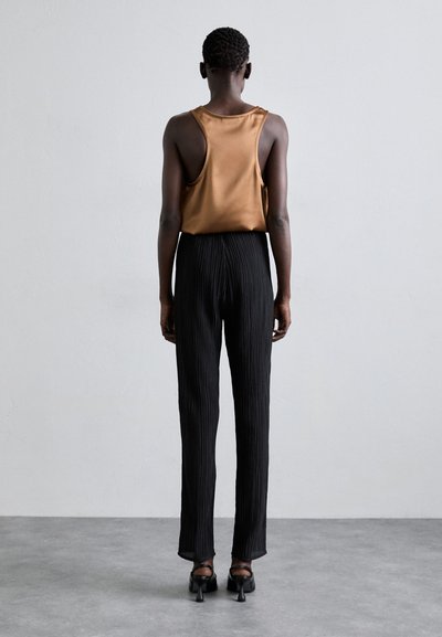 Top in satin bronzo con schiena a racer, abbinato a pantaloni larghi plissettati neri. Entrambi i capi presentano texture morbide e un design minimalista.