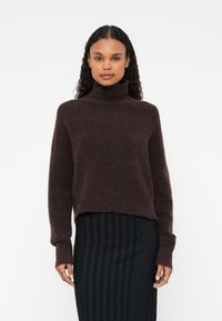 Burgundy polokrage tröja i mjukt, texturerat material, med kort design och långa ärmar, tillsammans med en texturerad svart kjol.
