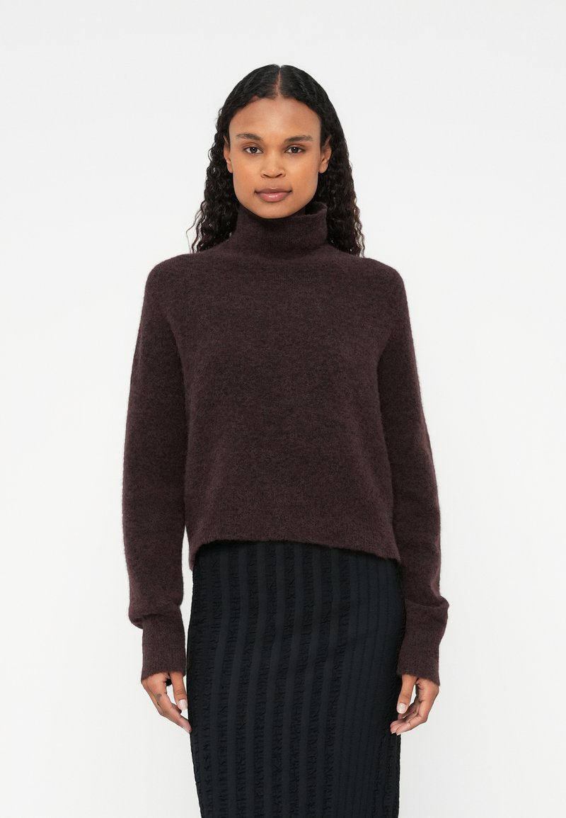 Burgundy polokrage tröja i mjukt, texturerat material, med kort design och långa ärmar, tillsammans med en texturerad svart kjol.