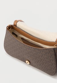 Sac bandoulière marron à motifs avec des accents en cuir fauve, une quincaillerie dorée et une doublure en toile. Dispose d'une fermeture à pression magnétique.