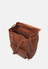 Sac seau en cuir synthétique marron avec une fermeture à cordon, une poche intérieure et une poche zippée à l'avant. Texture lisse avec quincaillerie dorée.