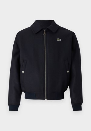 Veste zippée marine avec un col, des poignets côtelés, des poches latérales et un petit logo vert sur la poitrine gauche. Tissu texturé.