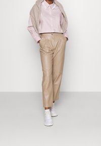 Beige faux læderbukser med en afslappet pasform, hvide sneakers og en lyserød stribet skjorte med krave lagdelt med en beige striktrøje.