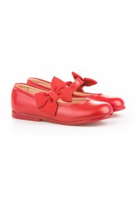 Par de zapatos tipo Mary Jane rojos para niñas con grandes lazos de tela en las correas, suelas planas y punteras redondas sobre un fondo blanco.