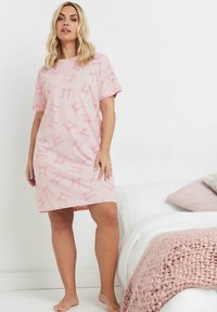 Camicia da notte in cotone rosa con un motivo ripetuto di fiocchi rosa. Maniche corte e vestibilità comoda, che arriva a metà coscia.