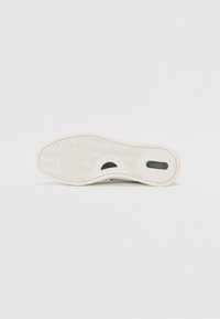 Semelle de chaussure en matériau caoutchouteux, dotée d'un motif de relief en chevrons, de couleur blanche, et d'un découpage circulaire pour une meilleure traction et un meilleur soutien.