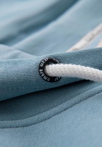 Gros plan sur un cordon tressé blanc passant à travers un œillet métallique noir sur un vêtement en tissu bleu clair.