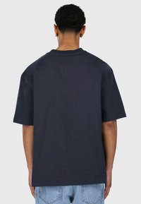 Czarny bawełniany t-shirt z krótkimi rękawami, luźny krój i prosty dół. Bez widocznych nadruków ani logo, minimalna tekstura.