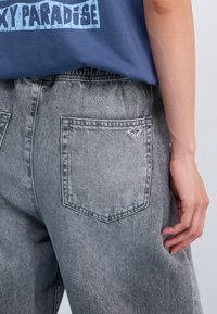 Grå denimbukser med en falmet vask, som har et klassisk fem-lomme design og et lille logomerke på baklommen.