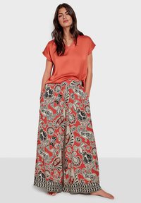 Rotes Satin-Top mit kurzen Ärmeln, kombiniert mit weit geschnittenen, gemusterten Hosen mit floralen Designs in Schwarz und Weiß, die am Saum mit einem schwarzen Rand abgeschlossen sind.