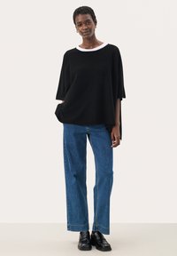 Haut noir à manches courtes avec bord blanc, associé à un jean bleu à jambes droites et des chaussures noires. Design minimaliste et coupe décontractée.