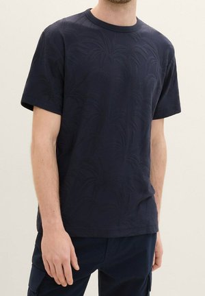 T-shirt bleu marine en coton avec un motif de feuilles de palmier texturé, manches courtes et col rond côtelé. Stylisé avec un pantalon cargo bleu marine.