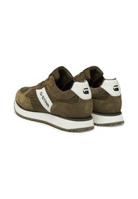 Olivzaļas krāsas sporta apavi ar zamšādas un tekstila augšpusi, baltas krāsas akcentiem un polsterētu apkakli. Aprīkoti ar teksturētu zoli labākai saķerei. G-Star zīmola logo.