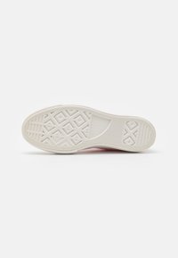 Spodní část bílé tenisky Converse All Star s diamantovým a pruhovaným vzorem na hladkém pozadí.