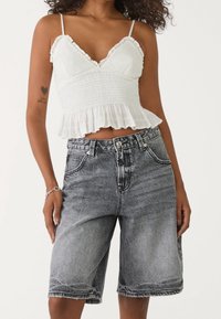 Witte gesmokte cropped top met gerimpelde randen, gecombineerd met zwart denim bermuda shorts met hoge taille, voorzien van een vervaagde wassing en rafelige zoom.