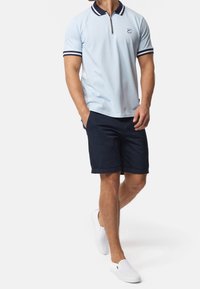 Jasnoniebieska koszulka polo z zamkiem przy kołnierzyku, granatowe paski na rękawach, w połączeniu z granatowymi szortami i białymi butami wsuwanymi.
