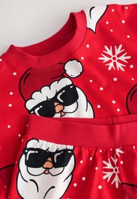 Tenue en coton rouge avec un motif de Père Noël portant des lunettes de soleil, des pois blancs et des flocons de neige. Le col et la ceinture côtelés assurent un ajustement confortable.