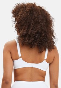 Soutien-gorge blanc avec bretelles réglables, fermeture à crochets au dos, matériau doux et texture lisse. Pas de motifs ni d'accents visibles.