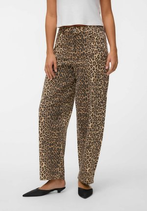Donna che indossa pantaloni a gamba larga a vita alta con stampa leopardata, top corto bianco e scarpe slip-on nere con tacco basso e punta, in piedi su sfondo bianco.