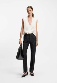 Weiße ärmellose Bluse mit tiefem V-Ausschnitt, kombiniert mit dunklen geraden Jeans. Eine schwarze Handtasche und spitze Ballerinas runden das Outfit ab.