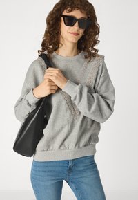 Sweat-shirt gris avec des accents en dentelle, col rond et poignets côtelés. Associé à un jean bleu et un sac à bandoulière noir.