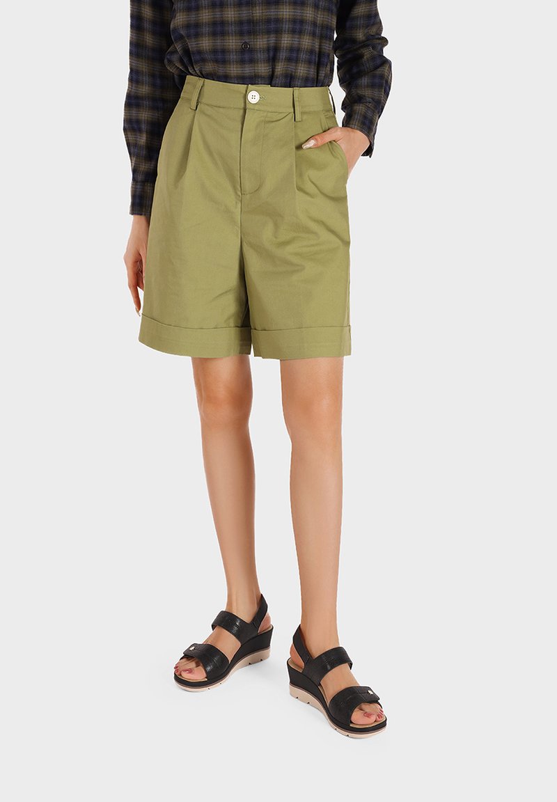 Pantaloni corti in cotone khaki con vita alta, tasche laterali e orlo risvoltato, abbinati a sandali neri con due cinturini e tacco a zeppa.