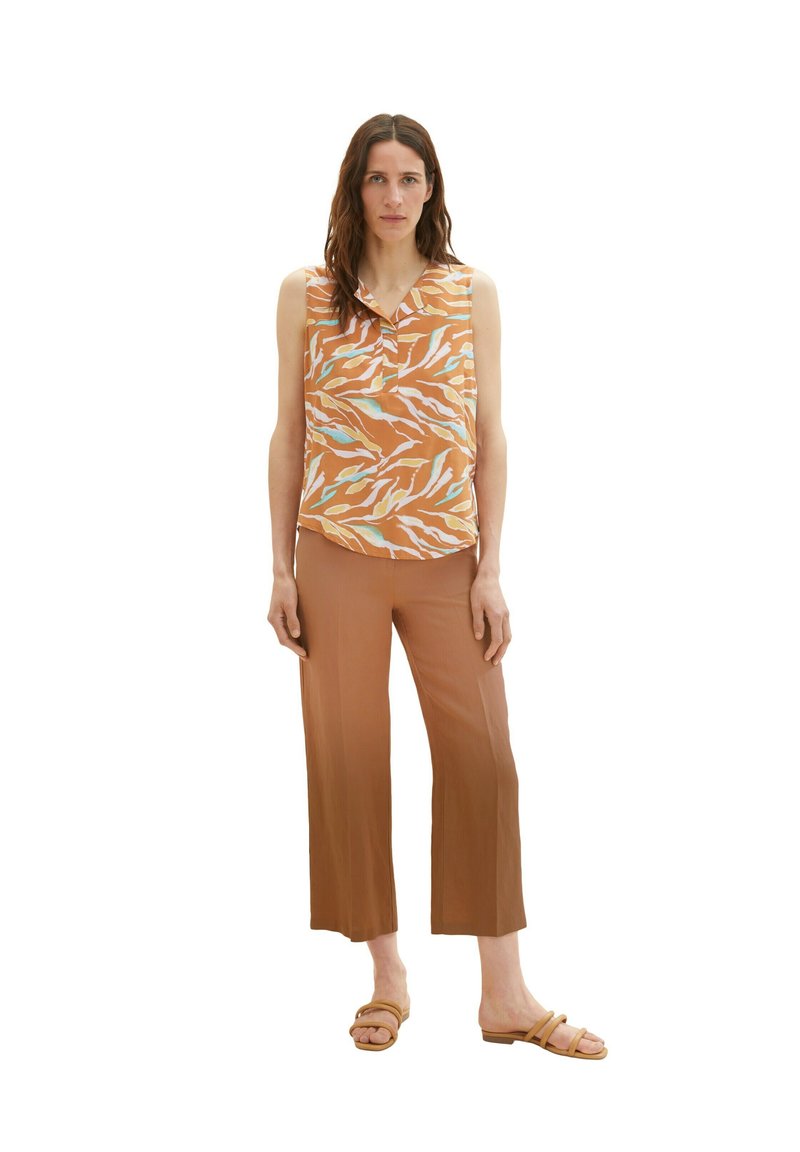 Sleeveless top with orange and white abstract pattern, paired with brown wide-leg pants and tan sandals. Smooth fabric, casual design.