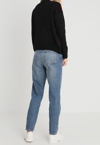 Pull noir en maille avec un col rond, associé à un jean en denim bleu taille haute et des baskets blanches. Coupe décontractée et texture douce.