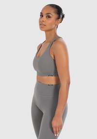 Grijze sportoutfit bestaande uit een getailleerde tanktop met brede schouderbanden en bijpassende high-waisted legging, beide in een gladde, matte textuur.