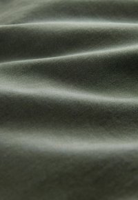 Pehme roheline kangas, millel on nähtav diagonaalne kudumise tekstuur ning õrnad voltid, mis loovad peeneid varje ja rõhutusi.