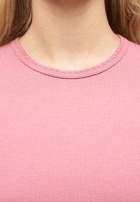 Κοντινή λήψη του λαιμού και του επάνω μέρους του στήθους ενός ατόμου που φοράει ένα ροζ  ριγέ μπλουζάκι με υφή και στρογγυλή λαιμόκοψη.