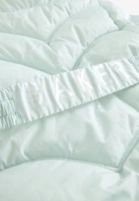 Svijetloplava puffer jakna s kviltanim dizajnom, koja ima glatku teksturu i elastičnu donju ivicu. Oznaka na kojoj piše "BAKER by TED BAKER" je vidljiva.
