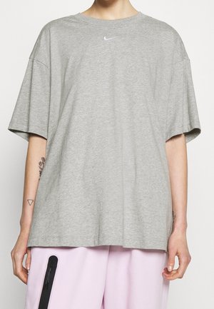 Osoba ubrana w luźny szary T-shirt Nike z krótkimi rękawami i jasnoróżowe spodnie z czarną pionową kieszenią na zamek.