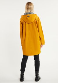 Cappotto impermeabile giallo con fodera del cappuccio grigia, maniche lunghe e tasche laterali. Presenta un taglio dritto e polsini con bottoni a pressione.
