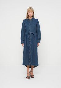 Jeanshemdjurk met lange mouwen, knoopsluiting, tailleband en een hoge-laag zoom. Donkerblauwe kleur met vervaagde accenten en kraagdetail.