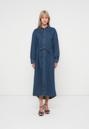 Kjole i denim med lange ermer, knappelukking, midjebånd og høy-lav kant. Mørk blå farge med falmede detaljer og krage.