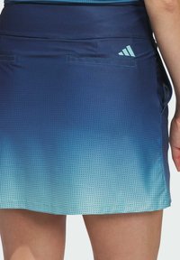 Blauwe sportrok met een gradatiepatroon, voorzien van een geperforeerde textuur, twee zijzakken en een klein logovoorstelling op de tailleband.
