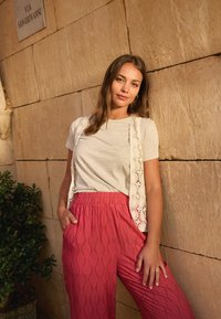 T-shirt gris clair superposé avec un débardeur en dentelle blanche, associé à un pantalon ample à motif rose vif avec un design de feuilles.