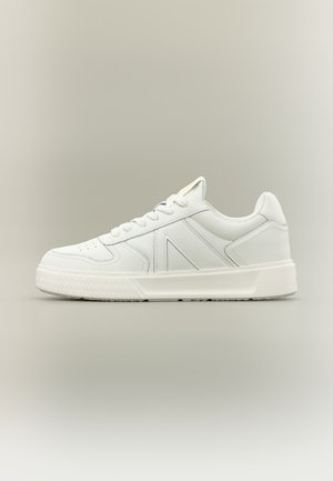 Bijela niska tenisica s vezicama sprijeda, debelim teksturiranim potplatom i dizajnom sašivenih panela, prikazana iz profila na neutralnoj pozadini.