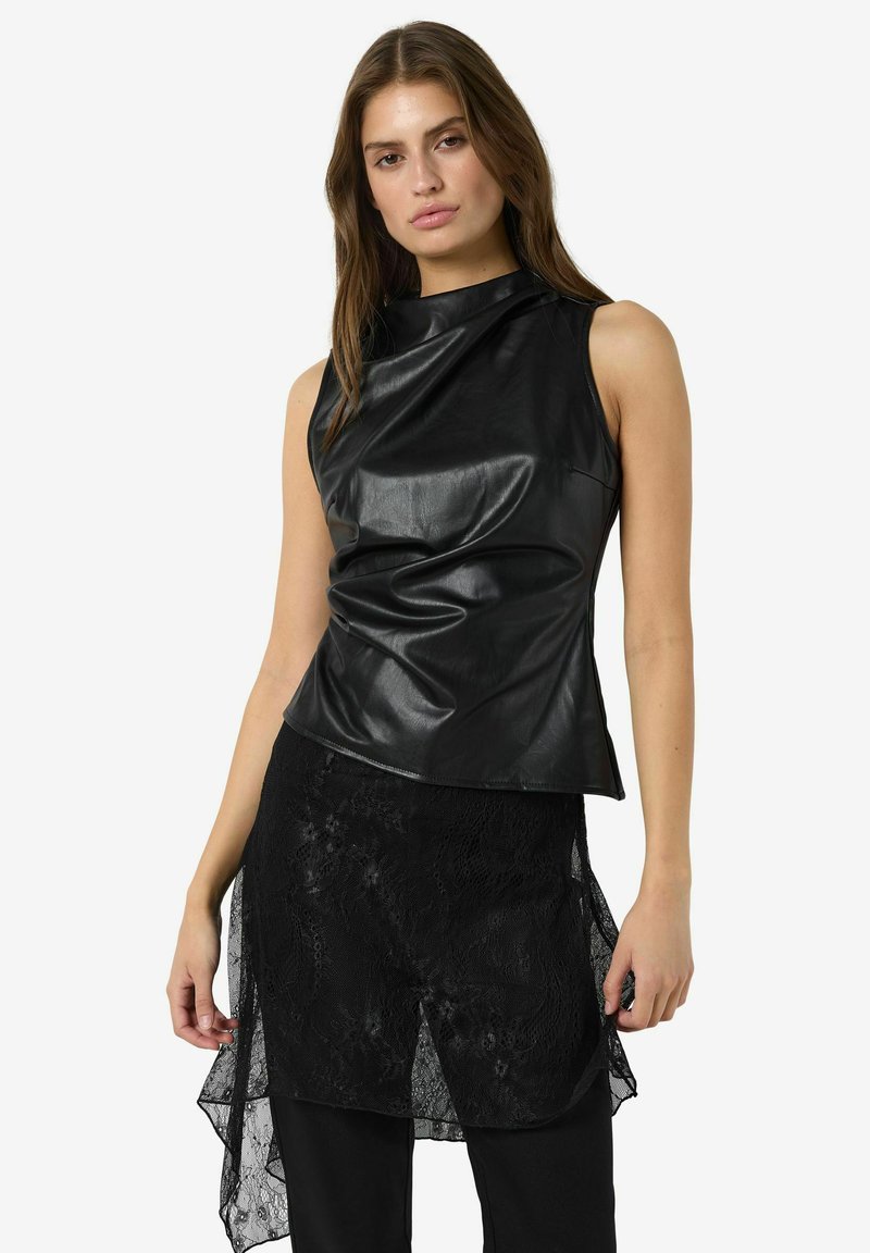 Svart läderlöst linne med hög krage och draperad design fram, i kombination med en genomskinlig svart spetskjol. Texturerad tyg synlig.