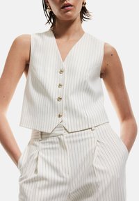 Gilet bianco a righe con scollo a V, design corto, caratterizzato da cinque bottoni dorati e una vestibilità sagomata, abbinato a pantaloni coordinati a righe.