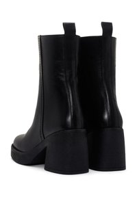 Botas de tobillo de cuero negro con un acabado suave, diseño ajustado y tacón de plataforma chunky. Cuenta con tiradores y costuras minimalistas.