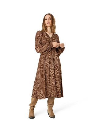 Braunes Tierfellmusterkleid mit langen Ärmeln und V-Ausschnitt. Mit geraffter Taille und einem fließenden Rock. Kombiniert mit beigen knielangen Stiefeln.