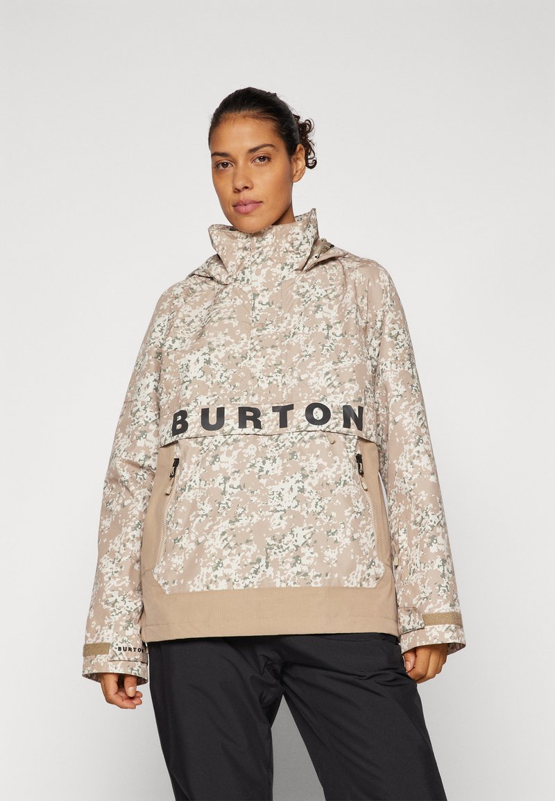 Beżowa kurtka w kwiatowy wzór z wysokim kołnierzem, czarnym logo "BURTON" i kieszeniami na zamek; charakteryzuje się luźnym krojem i teksturowanym materiałem.