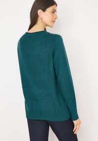 Maglione a maglia teal con maniche lunghe, scollatura rotonda, polsini e orlo a coste. Texture morbida e vestibilità rilassata, abbinato a jeans blu scuro.