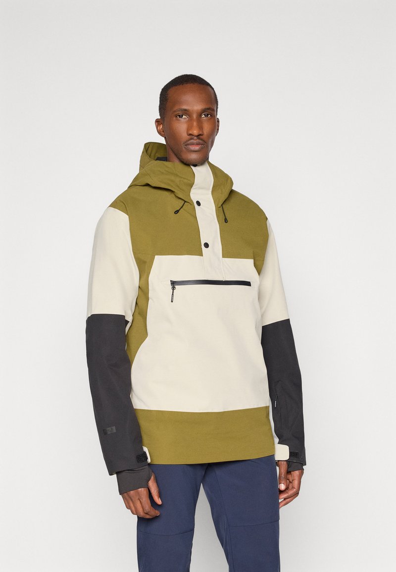 Vihreä ja kerma värilohkottu takki, jossa on huppu, etupainonappikiinnitys, vetoketjullinen rintatasku ja mustat hihat, joissa on tarranauhat.